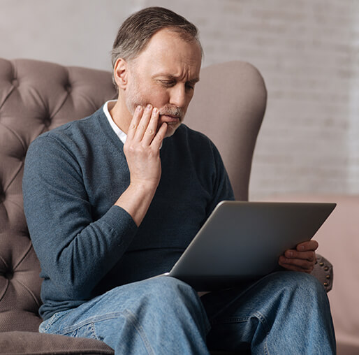 man holding his jaw while looking at a laptop